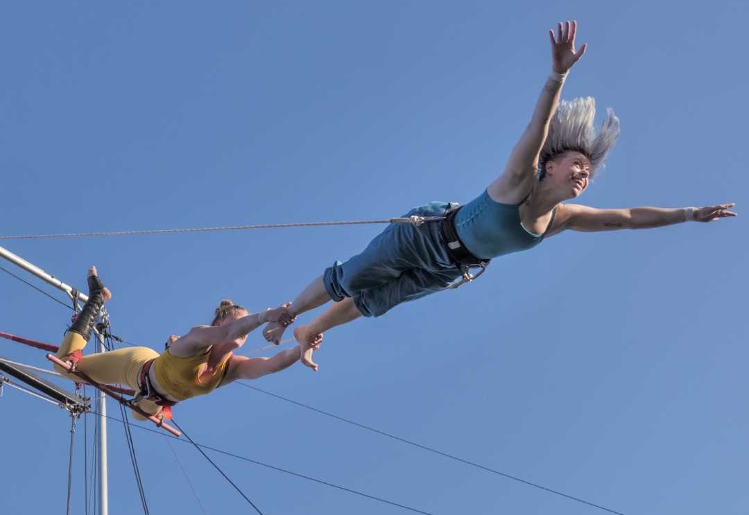 Two artists fly upside down on a large outdoor trapeze.